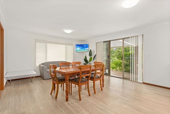 A dining area with a wooden table and chairs, a bench, and a TV on the wall.