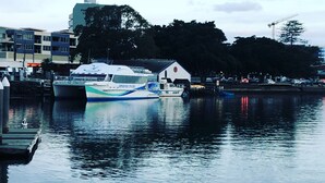 A marina with boats docked, a building with a crane, and a calm water body reflecting the sky. - Forster holiday home, linen included-WiFi- pets welcome-cafes,beach, golf, fish  (Forster)