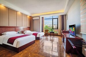 A hotel room with two beds, a TV, a desk, a chair, and a balcony with a view.