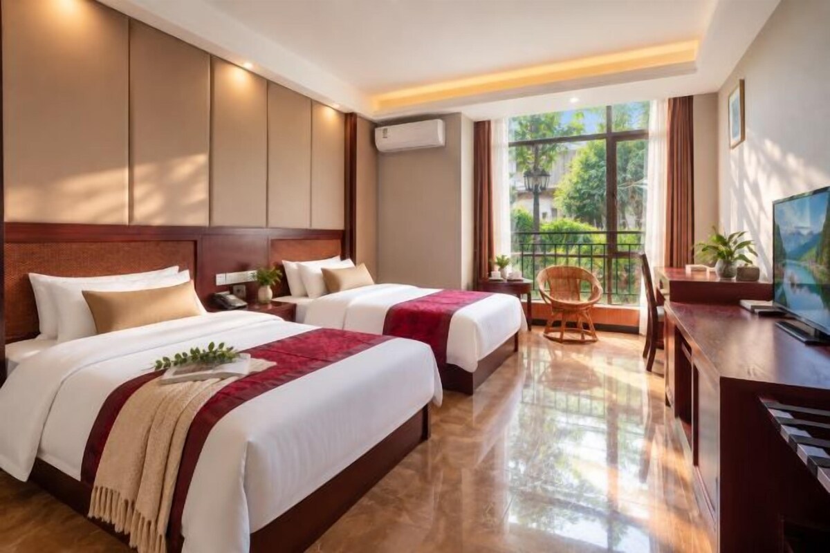 A hotel room with two beds, a desk, a chair, and a television.