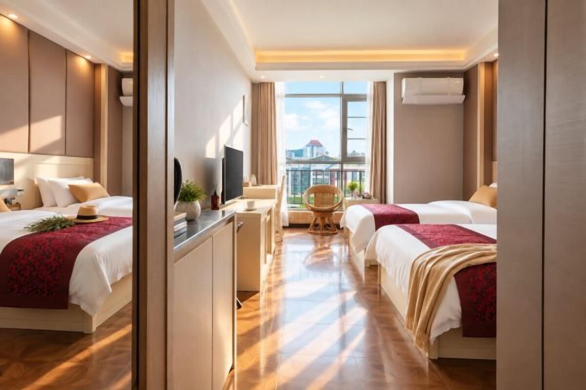 A hotel room with two beds, a desk, a chair, and a balcony with a view.