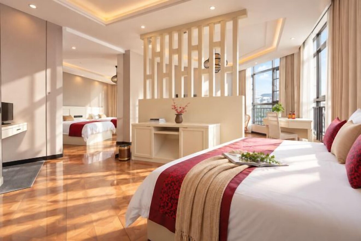 A hotel room with a large bed, a desk, a television, and a balcony with a view.