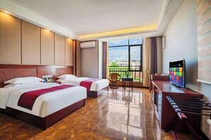 A hotel room with two beds, a TV, a desk, and a balcony with a view.