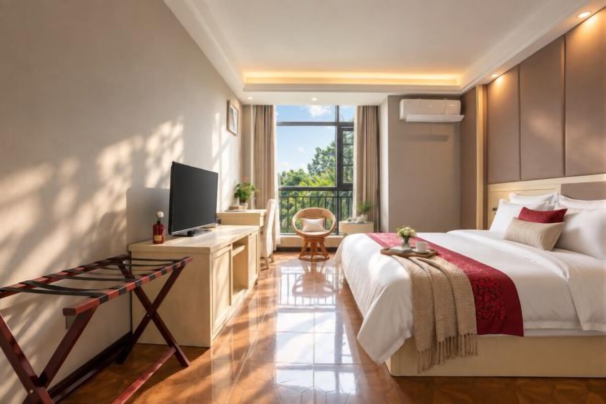 A hotel room with a bed, a desk with a TV, a chair, and a balcony with a view.