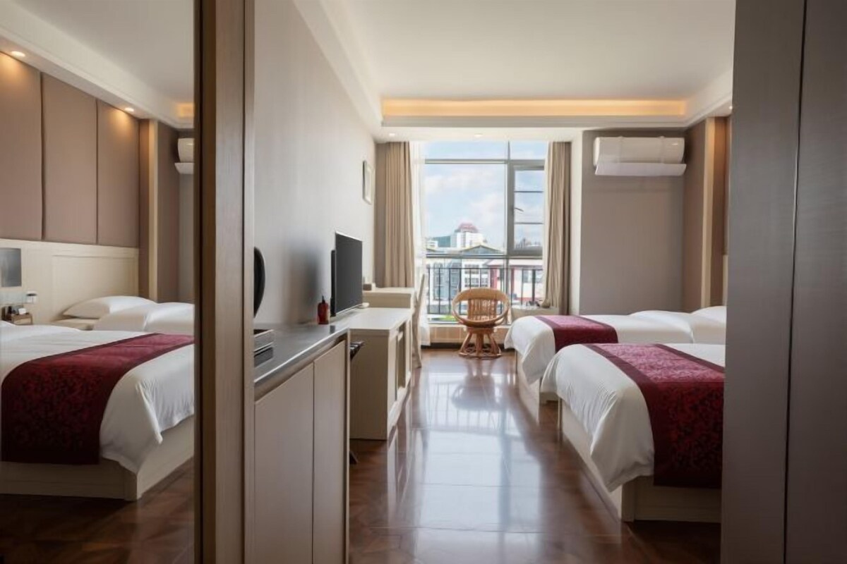 Ett hotellrum med två sängar, ett skrivbord, en stol, en tv och utsikt över staden.