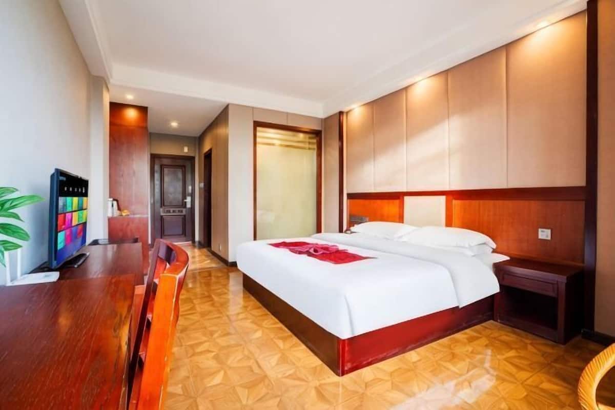 Een hotelkamer met een bed, nachtkastje en een televisie op een houten bureau.