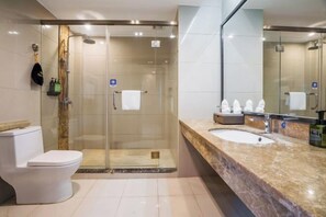 A modern bathroom with a glass-enclosed shower, a white toilet, and a marble countertop with a sink and mirror.