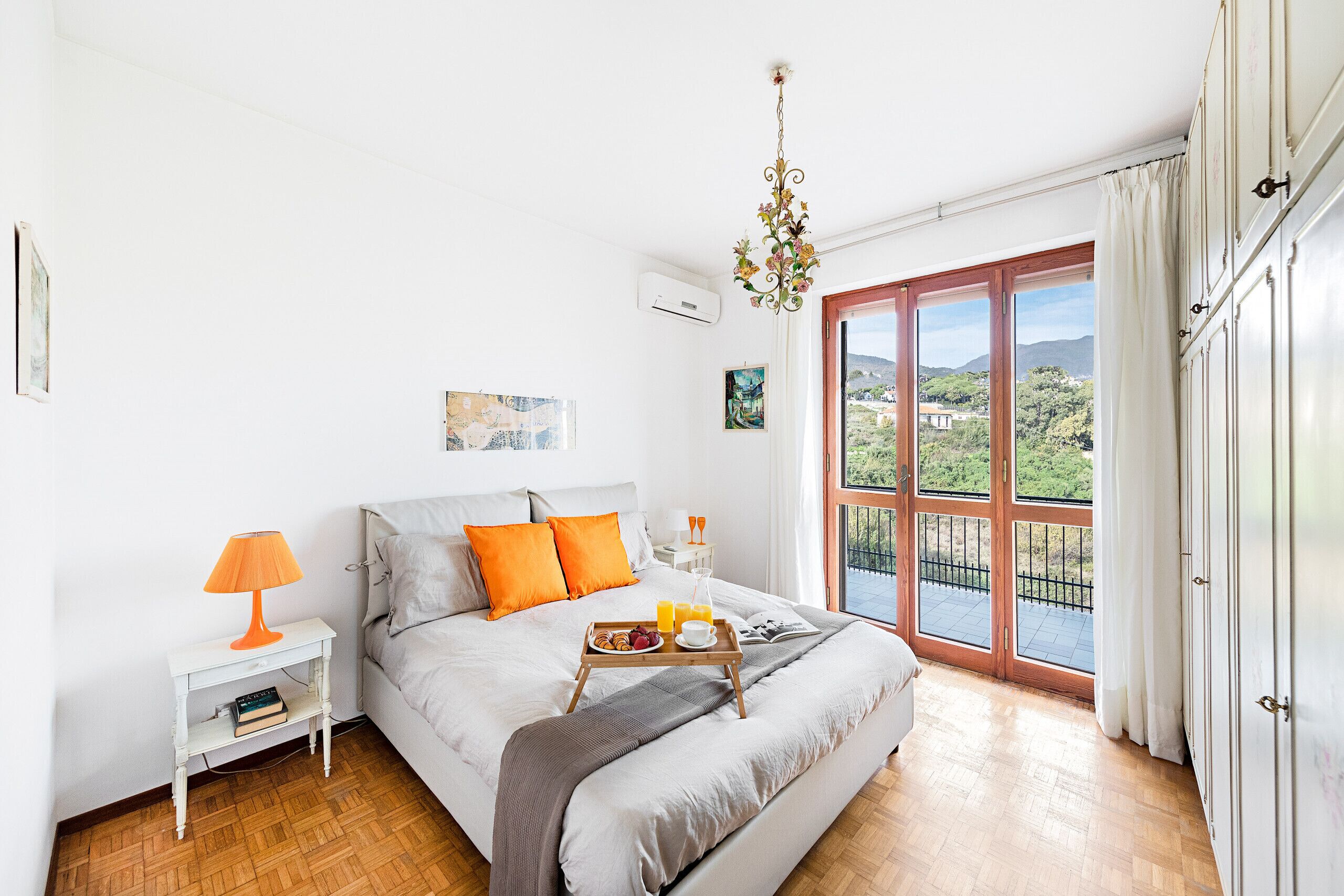 Une chambre avec un lit, une table de chevet avec une lampe, un plateau avec le petit-déjeuner et une grande fenêtre donnant sur un paysage verdoyant.