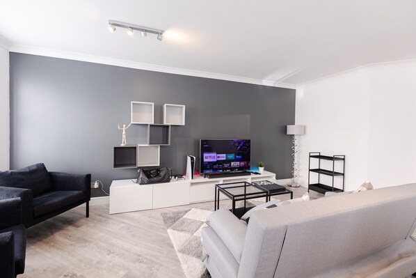 A modern living room with a grey sofa, a black armchair, a white sofa, a flat-screen TV, and a coffee table.