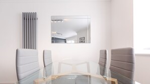 A modern meeting room with a glass table and leather chairs, a radiator, and a mirror on the wall. - Luxury, Modern Apartment w/ Netflix in Zone 2 (London)