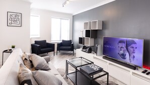 A modern living room with a large flat-screen TV, a sofa, a coffee table, and a minimalist design. - Luxury, Modern Apartment w/ Netflix in Zone 2 (London)