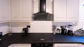 A modern kitchen with white cabinets, a black countertop, a built-in stove, a coffee maker, a blender, and a kettle. - Luxury, Modern Apartment w/ Netflix in Zone 2 (London)