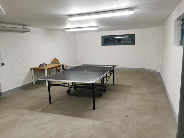 A room with a ping pong table, a wooden table with chairs, and a window. - Fewo-Strandmaennchen (Dahme)