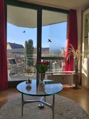A modern room with a glass table, a vase with flowers, and a view of a balcony with a red curtain. - Fewo-Strandmaennchen (Dahme)