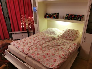 A bed with floral bedding, a bedside table, and a shelf with decorative pillows. - Fewo-Strandmaennchen (Dahme)
