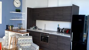 Une cuisine moderne avec des meubles de couleur sombre, un four encastré et un réfrigérateur noir. On y trouve également un coin repas avec une chaise à motifs et une petite table.