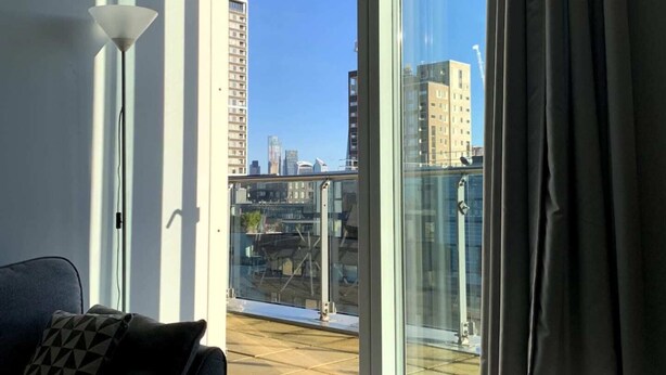 Un salon moderne avec un canapé, une lampe sur pied et une grande fenêtre donnant sur un paysage urbain.