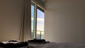 Une chambre avec une grande fenêtre, un lit recouvert d’une literie à motifs et une vue sur le paysage urbain.