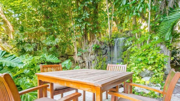 A wooden table and chairs set outdoors surrounded by lush greenery and a small waterfall. - SF 1Bed 1Bath Steps to Marina & CocoWalk in Grove (Miami)