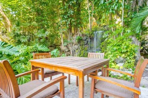 A wooden table and chairs set outdoors surrounded by lush greenery and a small waterfall. - SF 1Bed 1Bath Steps to Marina & CocoWalk in Grove (Miami)