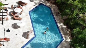 An octagonal pool with two people swimming, surrounded by lounge chairs and umbrellas, with lush greenery and a stone pathway. - SF 1Bed 1Bath Steps to Marina & CocoWalk in Grove (Miami)