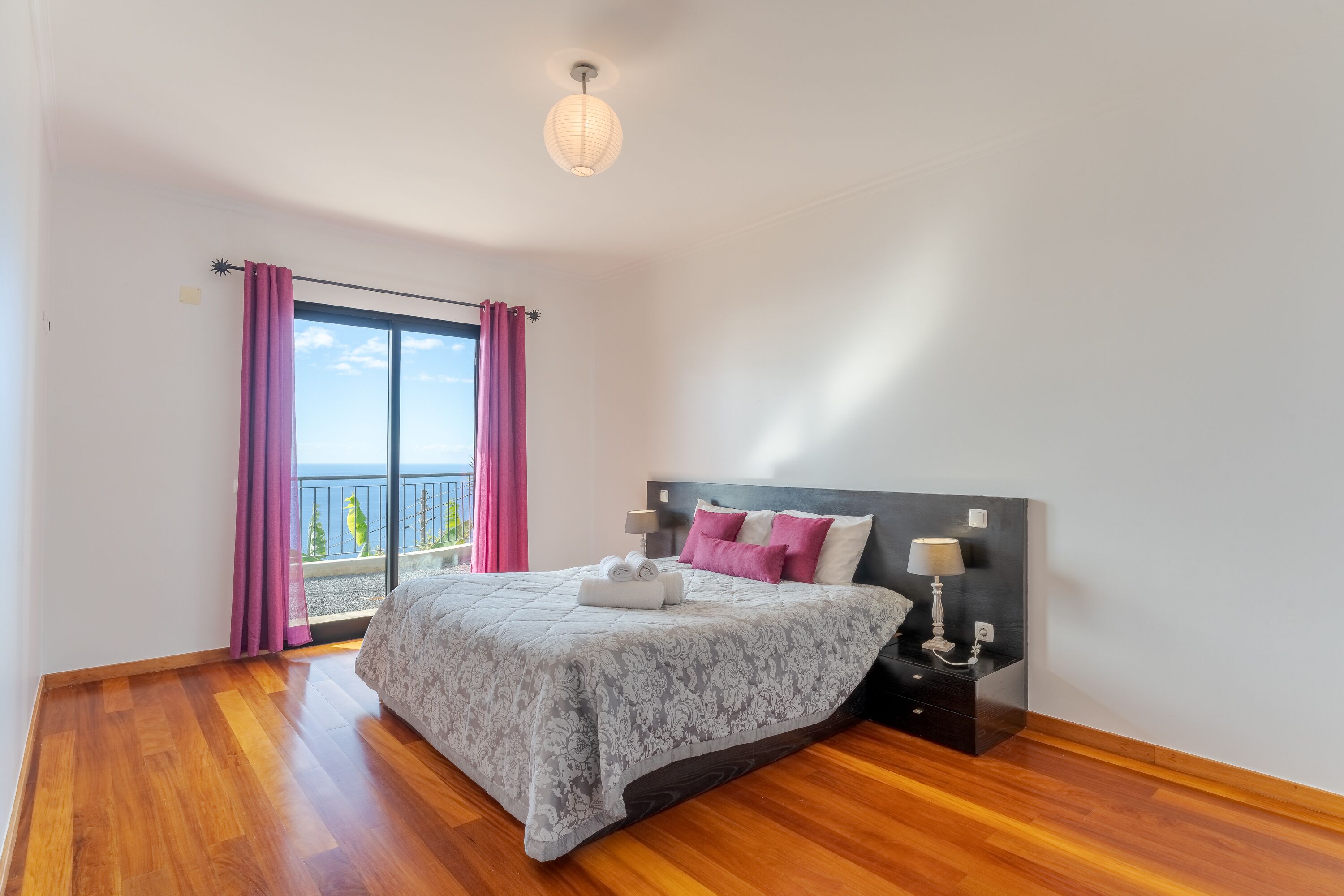 A bedroom with a bed, bedside lamps, a nightstand, and a view of the outdoors.