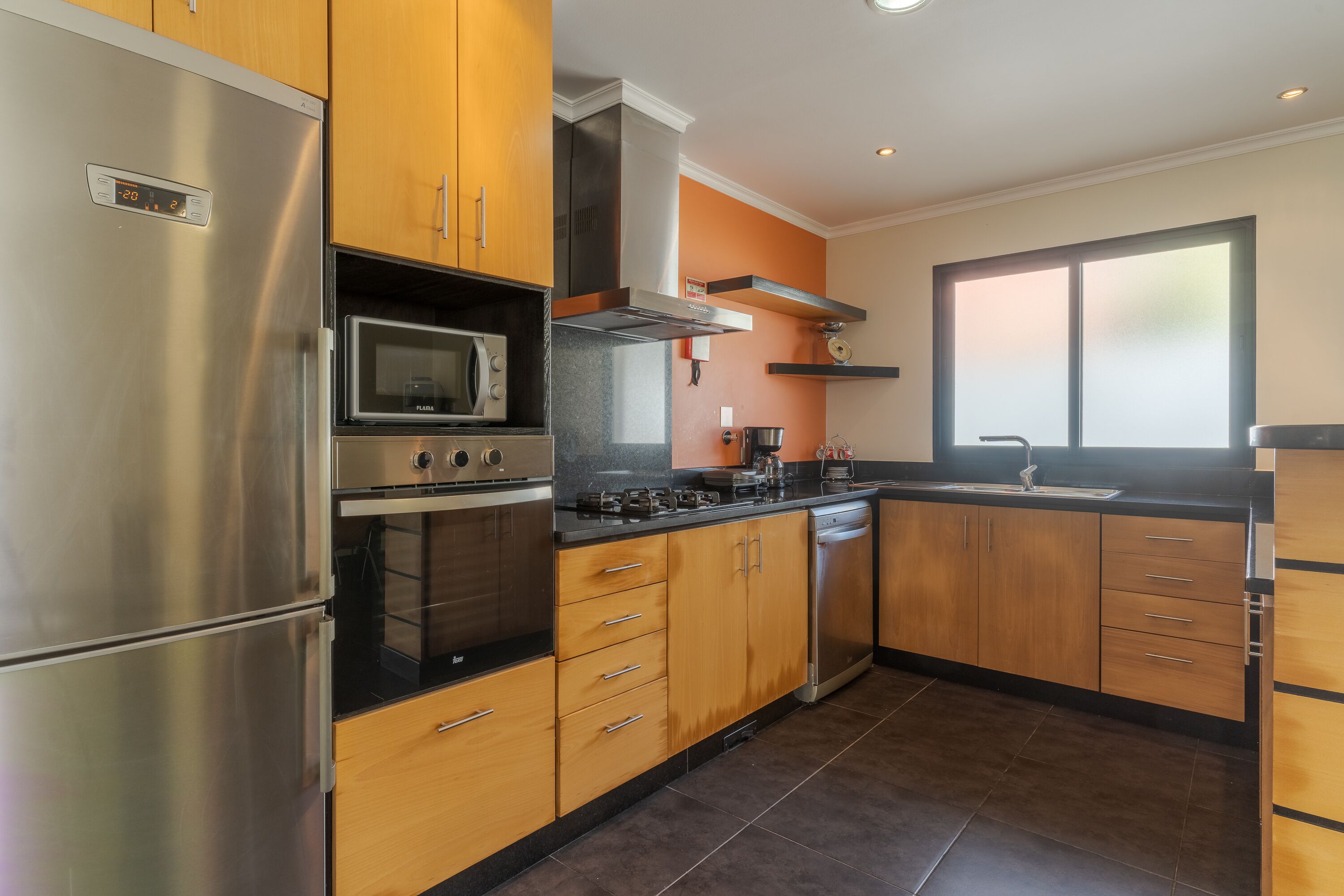 A modern kitchen with stainless steel appliances, wooden cabinets, and a large window providing natural light.