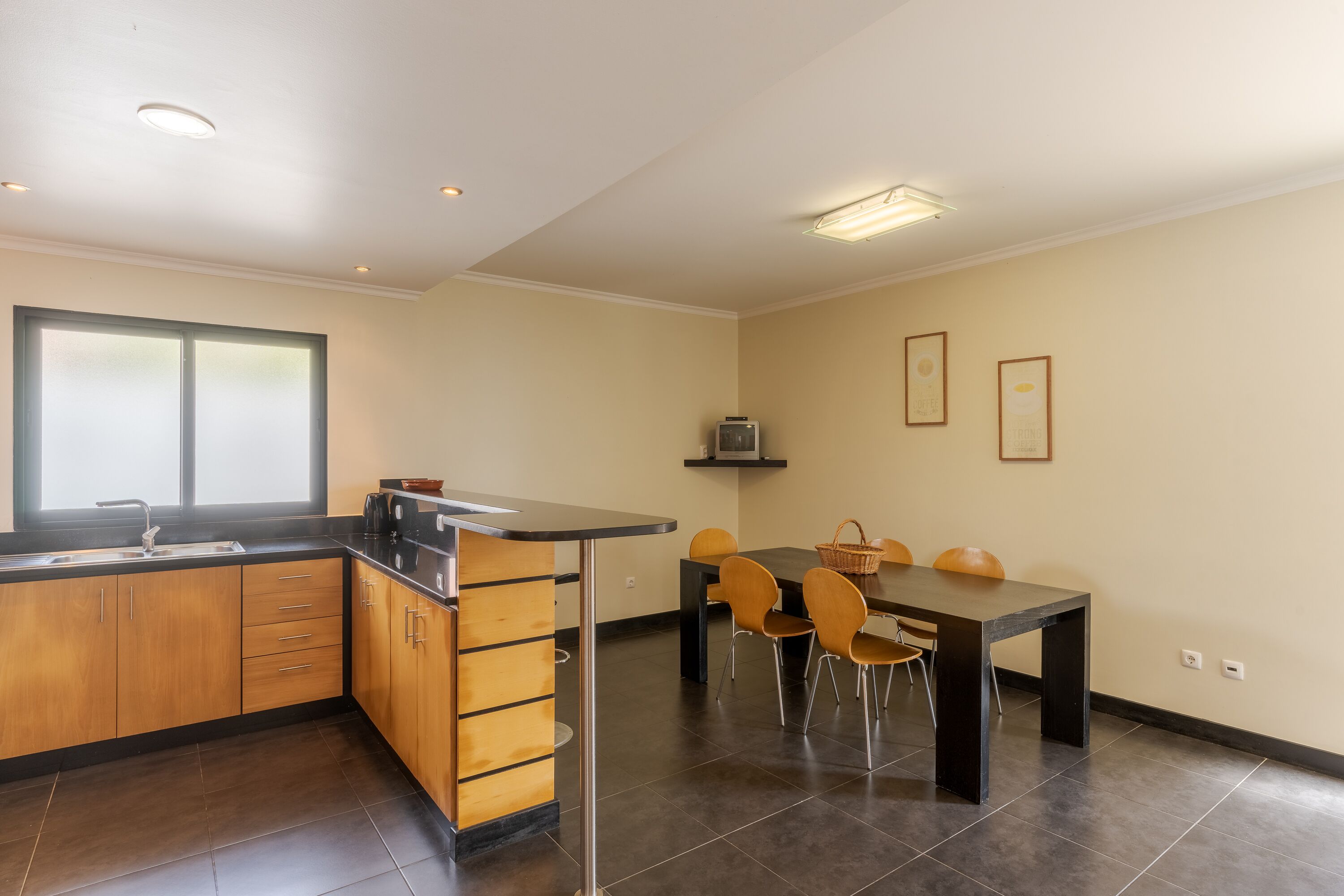 A modern kitchen with a dining area, featuring a black countertop, wooden cabinets, and a dining table with chairs.