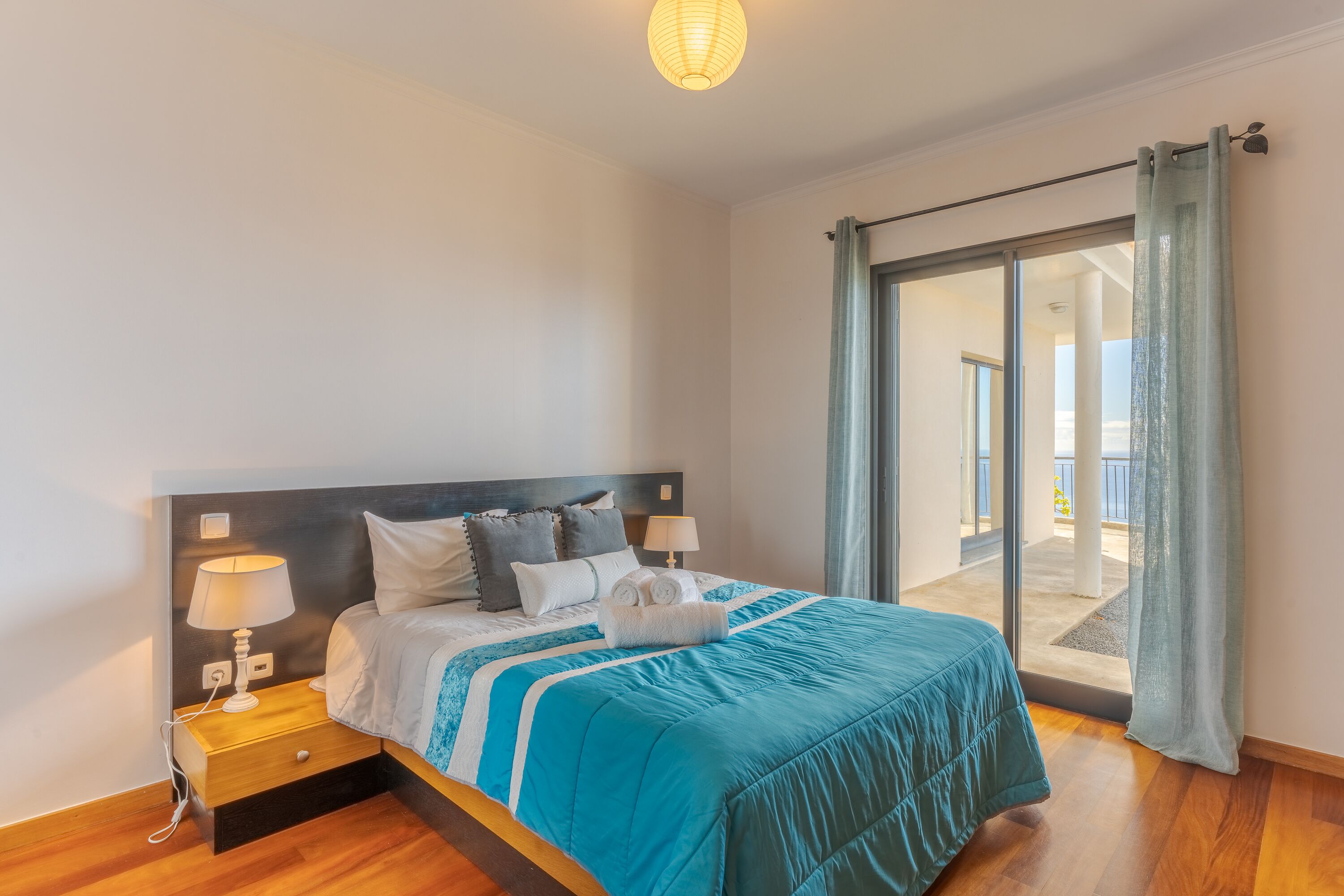 Ein Schlafzimmer mit Bett, Nachttischen, einer Lampe und Blick auf einen Balkon.