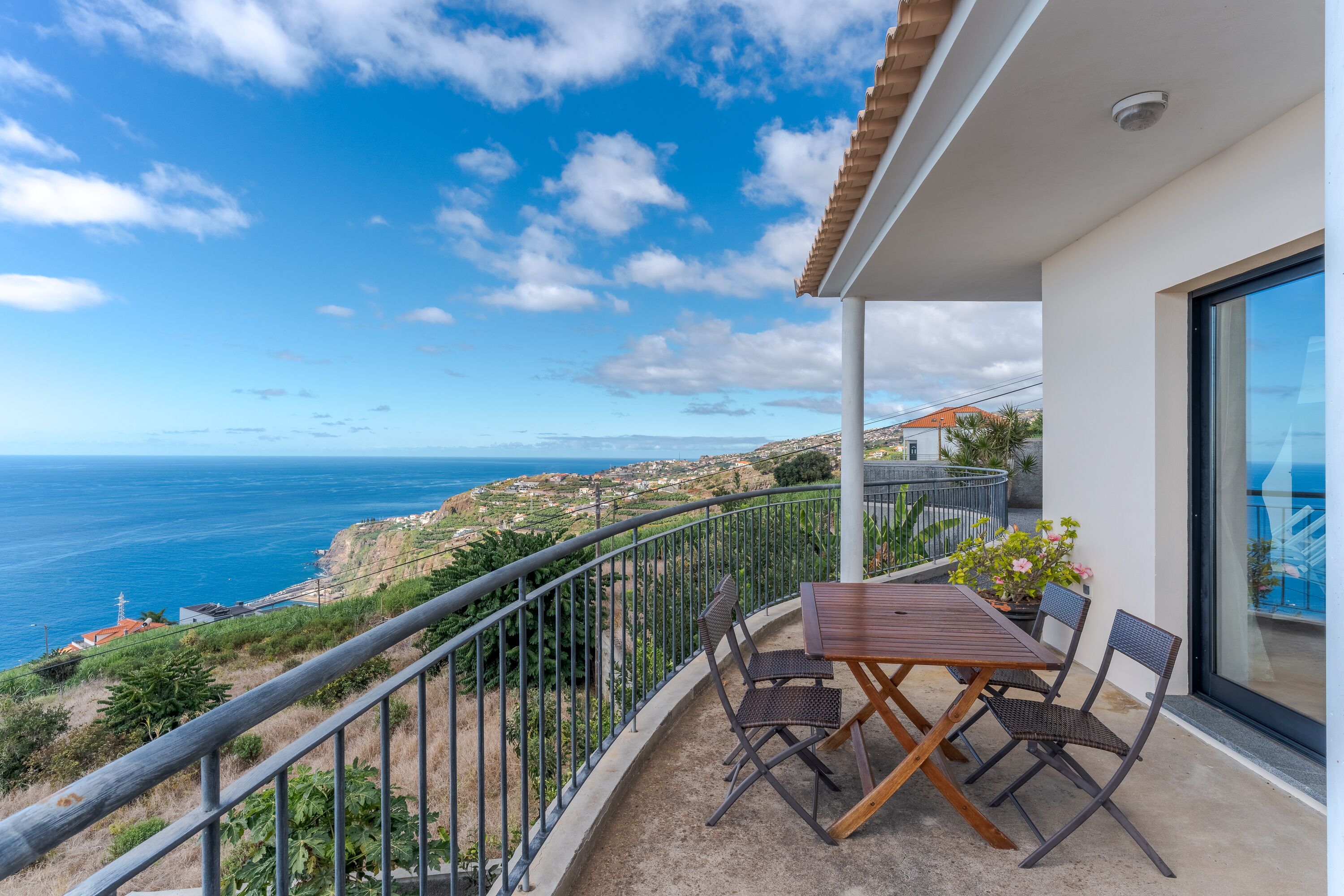 A balcony with a table and chairs overlooking a coastal view.