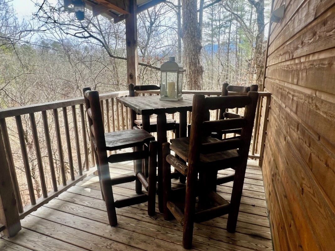 Un patio in legno con tavolo e sedie, una lanterna e vista sugli alberi.