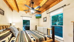 A bedroom with a large bed, a ceiling fan, a TV, and a window with a forest view. - GREAT EXPECTATIONS - 2 Bdrm/2 Bath, wood burning fireplace, secluded, Laurel Valley (Townsend)