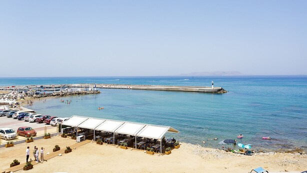 Eine Küstenlandschaft mit Strand, einer Mole und einem Restaurant mit Terrassensitzplätzen.