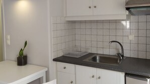 Eine kleine Küche mit weißen Schränken, einer schwarzen Arbeitsplatte, einer Edelstahl-Spüle und einer Wandleuchte.