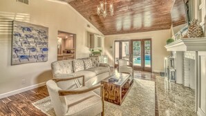A spacious living room with a wooden ceiling, a large painting, a fireplace, and a view of the outdoors. - 2-Min Walk to Beach, Free Pool and Spa Heat, Family & Dog-Friendly, Sleeps 17, Kids' Loft (Hilton Head Island)