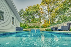 A swimming pool with a pergola, wicker furniture, and a wooden fence.