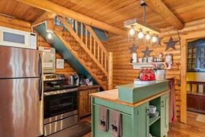 Cocina de cabaña de troncos con un refrigerador de acero inoxidable, una estufa y una encimera tipo isla verde.