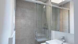 Un baño moderno con cabina de ducha de vidrio, lavabo blanco y un espejo grande.