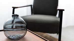 Un florero de vidrio transparente sobre una mesa de madera, con una silla negra moderna al fondo.