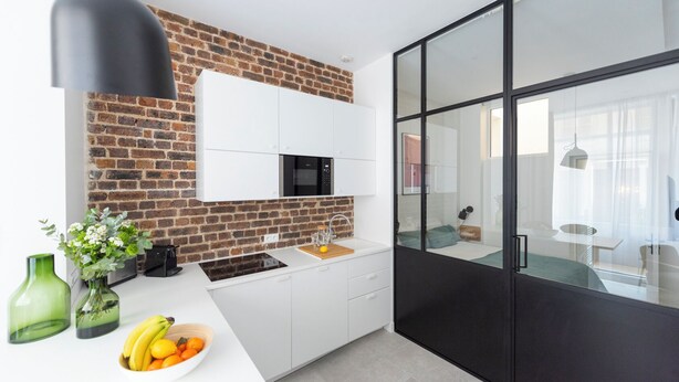 Una cocina moderna con pared de ladrillo, armarios blancos, un microondas negro y un ventanal grande.