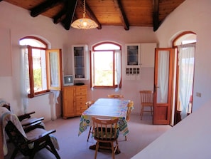 A dining area with a table set for four, wooden chairs, a television on a cabinet, and a window with curtains.
