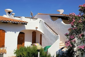 A white building with terracotta roof tiles, wooden doors, and a small balcony.