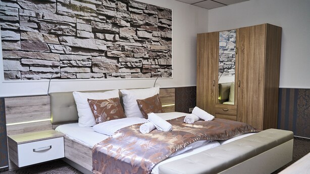A modern bedroom with a stone wall, a wooden wardrobe, and a neatly made bed. - Hotel Maximo (Pinneberg)