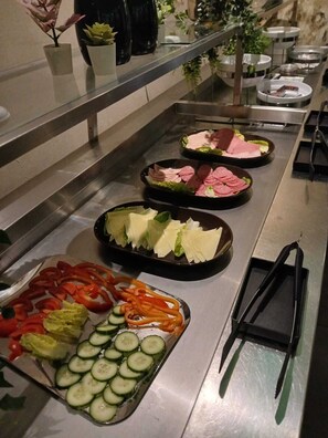 A buffet setup with various food items including sliced meats, cheeses, and vegetables.