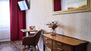 A hotel room with a wooden desk, a chair, a TV mounted on the wall, and a vase with flowers on the desk. - Hotel Maximo (Pinneberg)