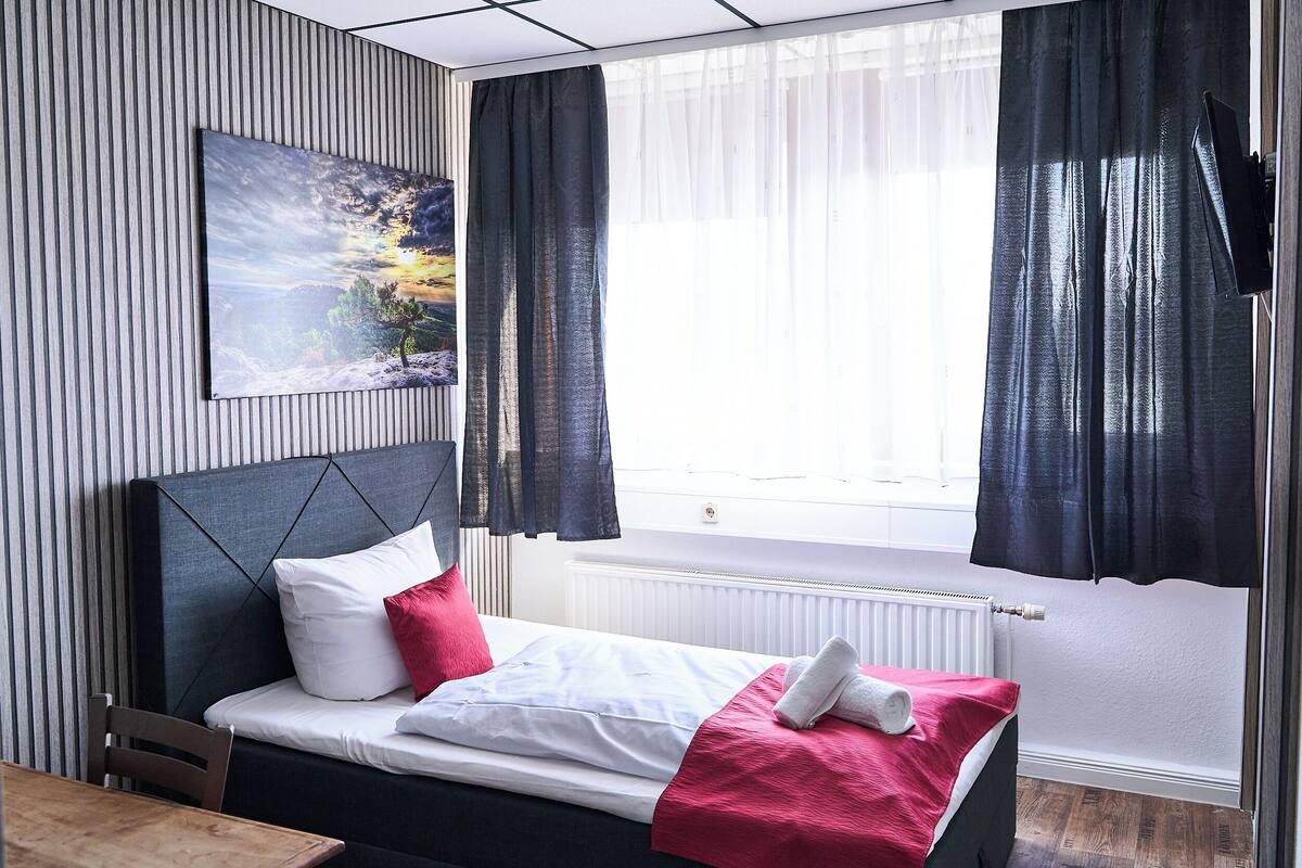 A modern bedroom with a bed, a headboard, a window with curtains, a radiator, and a painting on the wall.
