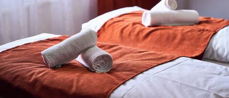Quarto de hotel com duas camas, cada uma com uma almofada branca e uma toalha branca enrolada.