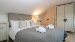 A bedroom with a large bed, a bedside table, a nightstand, a wardrobe, and a wall-mounted lamp. - Bwthyn Cerrig Man (Pwllheli)