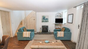 A living room with two teal sofas, a wooden coffee table, and a staircase leading to another level. - Bwthyn Cerrig Man (Pwllheli)