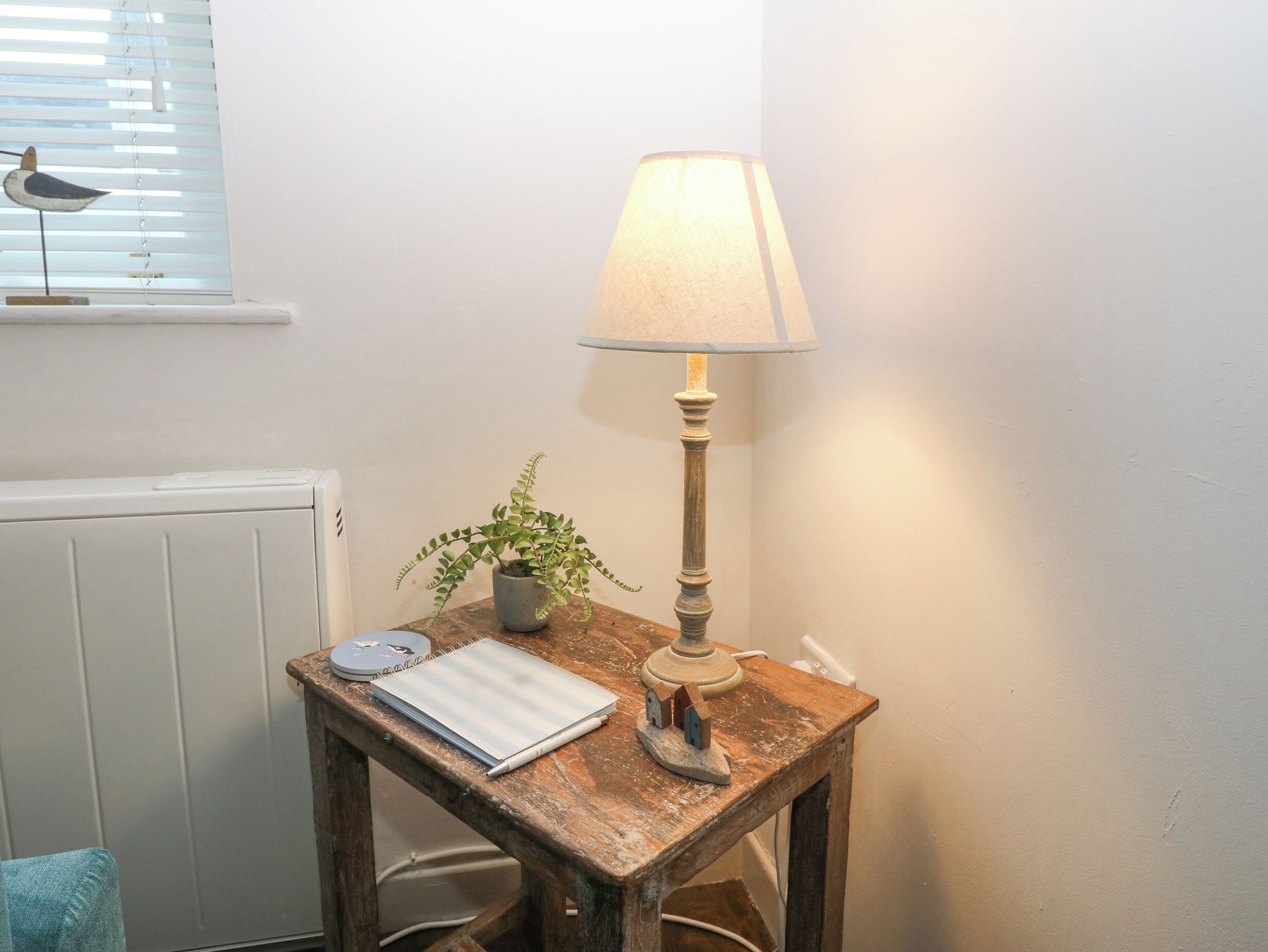 A small wooden table with a lamp, a notebook, and a potted plant.